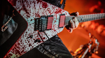 Guitarra eléctrica de diseño angular con acabado rojo salpicado, en directo